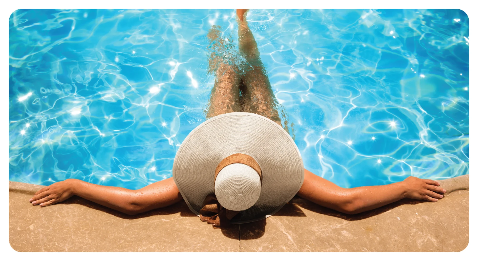 Woman in a wide-brimmed sun hat relaxing at the edge of a sunlit pool